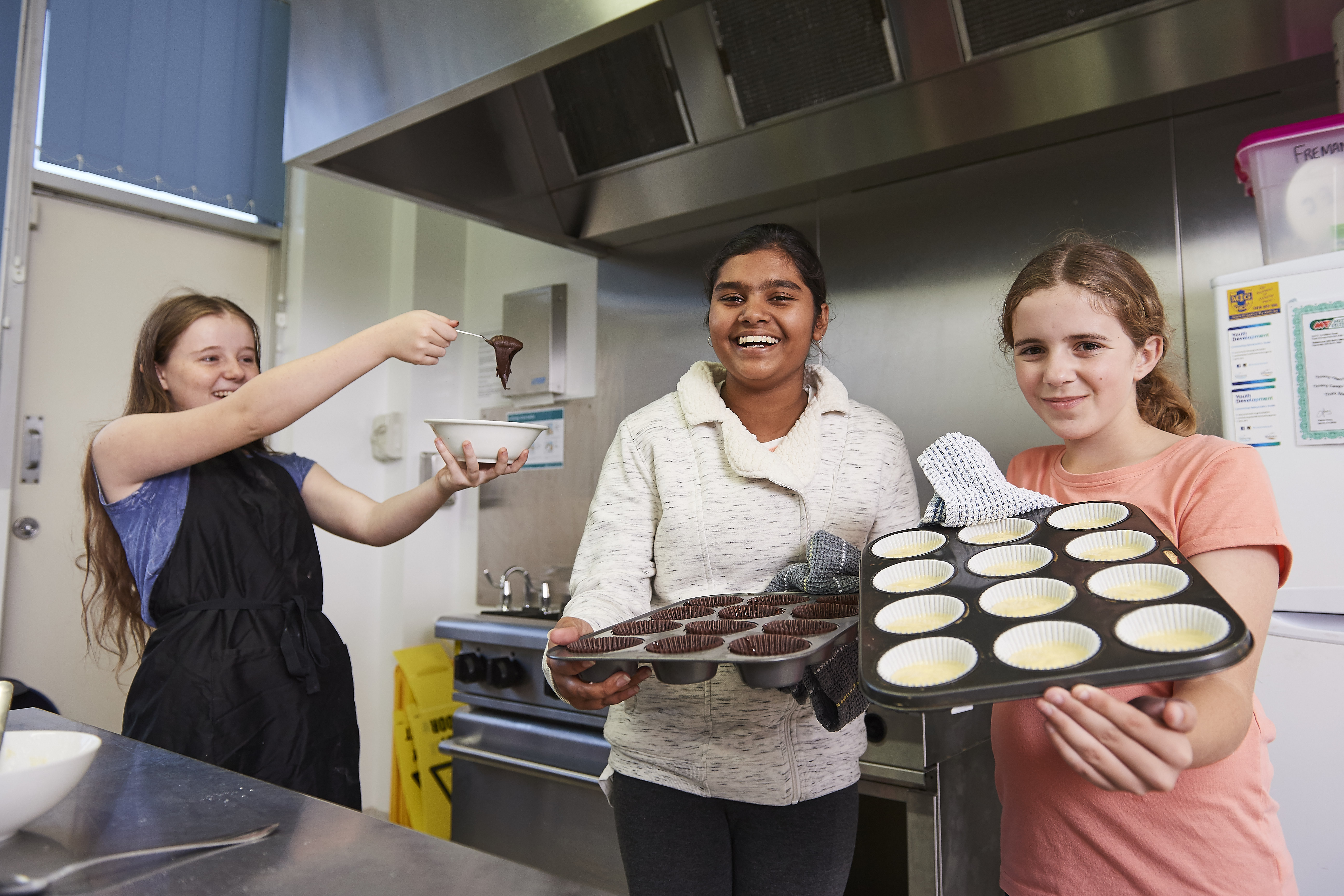 Three teenage girls cooking cupcakes in a kitchen